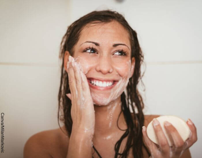 Foto de una mujer en la ducha lavando su rostro con un jabón para el cuidado facial