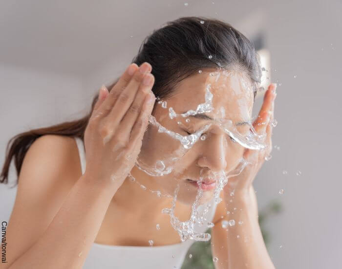 Foto de una mujer lavando su rostro en el lavamanos con una manotada de agua