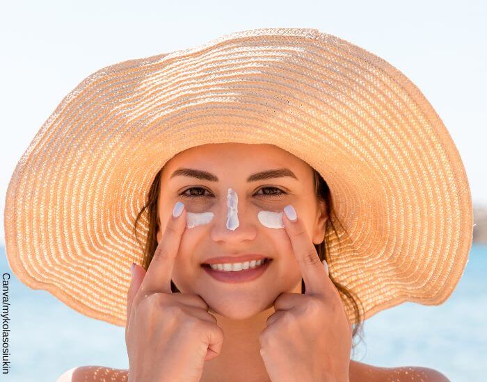 Foto de una mujer en la playa aplicando bloqueador solar en su rostro
