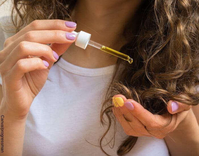 Foto de una mujer aplicando aceite de argán con un gotero a las puntas de su cabello