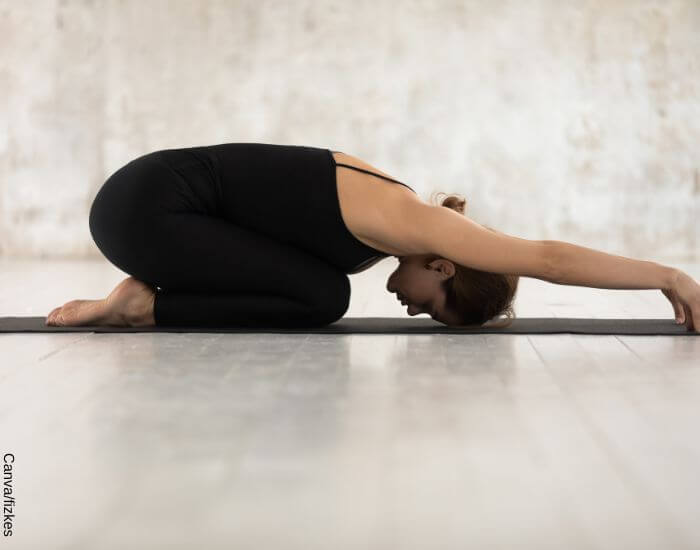Foto de una mujer sobre un tapete de yoga haciendo la pose del niño