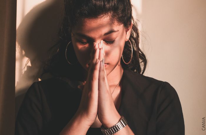 Foto de una mujer rezando con los ojos cerrados y las manos juntas