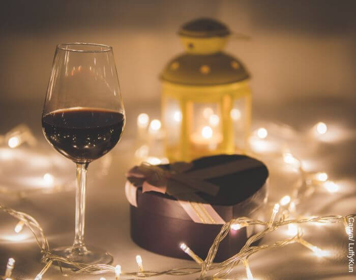 Foto de una copa de vino, luces y un regalo en representación de la carta de amor ideal para cada momento de la relación