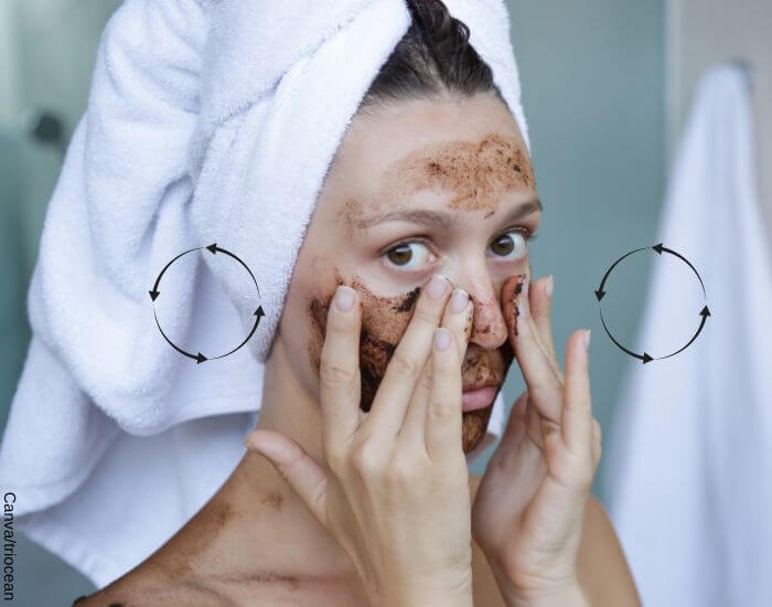Foto de una mujer en el baño aplicando una mascarilla de café para la cara y masajeando su rostro con movimientos circulares