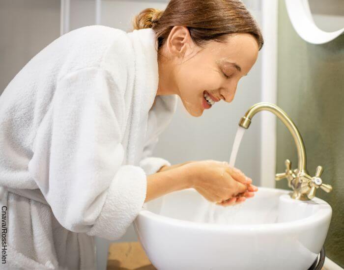 Foto de una mujer frente al lavamanos enjuagando con abundante agua la mascarilla de café para la cara que se aplicó