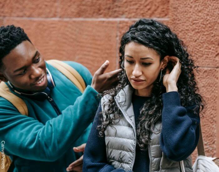 Foto de una mujer acomodando su cabello detrás de su oreja de forma insegura mientras su amigo le habla