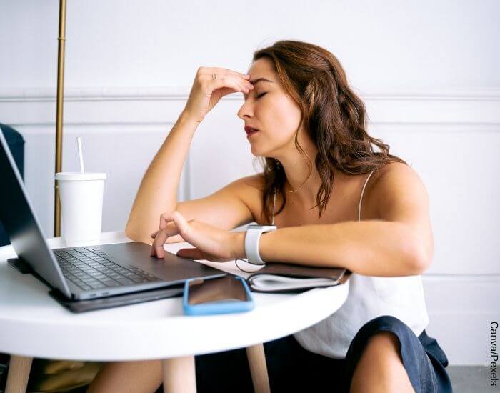 Foto de una mujer frente a un computador con una mano en su frente en señal de estrés