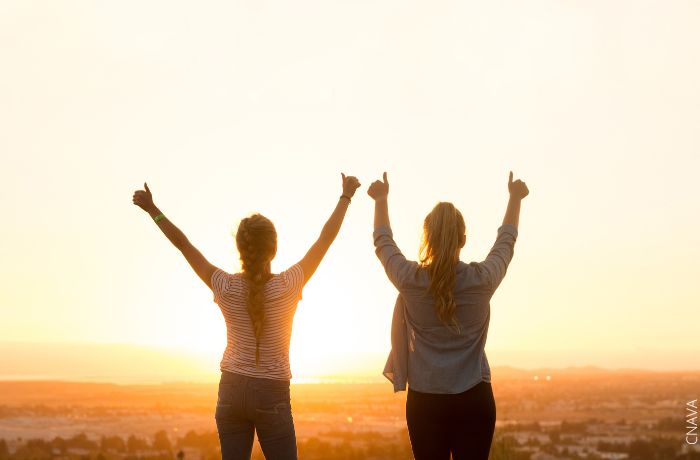 Foto de dos mujeres frente al amanecer levantando las manos y los pulgares