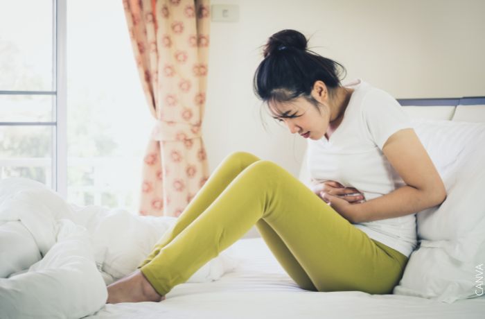 Foto de una mujer sentada en la cama con la manos en el estómago