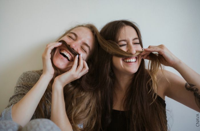 Foto de dos amigas riéndo y jugando con su cabello