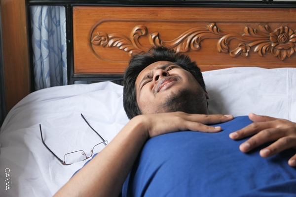Foto de un hombre recostado en la cama con cara de dolor.