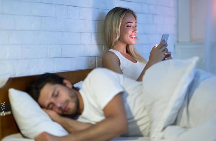 Foto de una mujer mirando su telefono mientras su pareja duerme