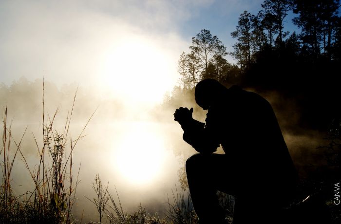 Foto de un hombre rezando frente a un lago al amanecer