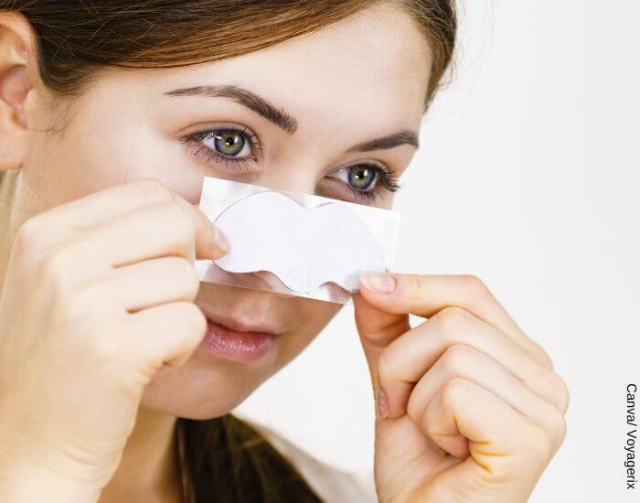 Foto de una mujer con una tira para quitar espinillas sobre su nariz para representar cómo quitar los puntos negros de la cara