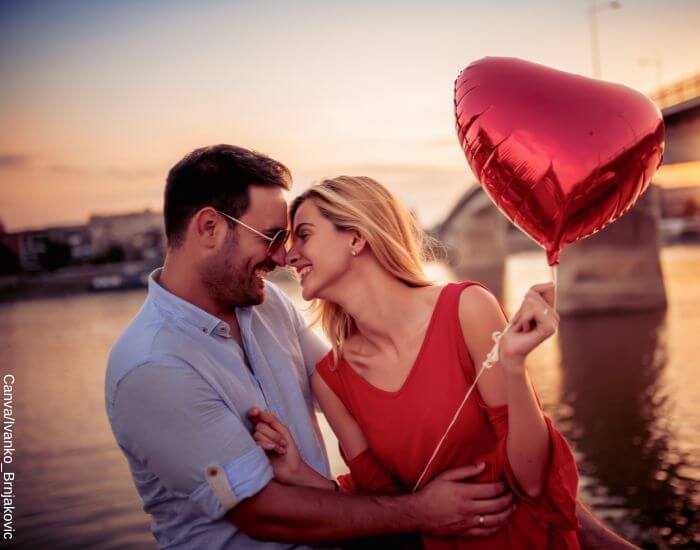 Foto de una pareja frente a un lago con un globo en forma de corazón