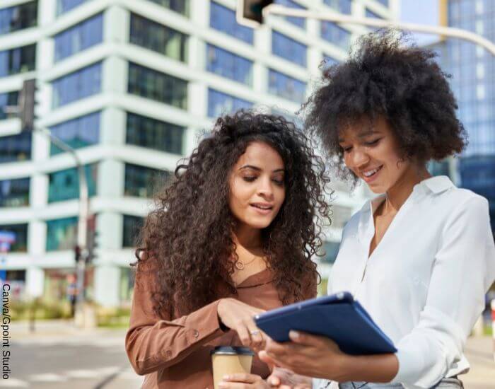 Foto de dos mujeres de carácter fuerte según su signo hablando en la calle mientras miran una tablet y toman café