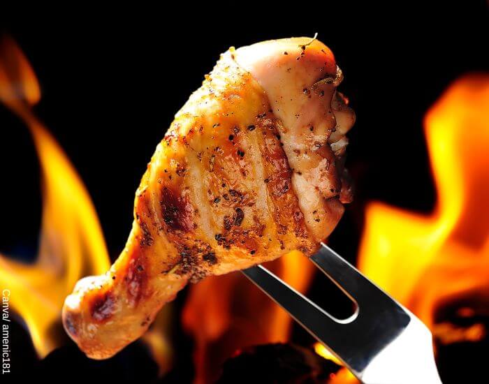 Foto de un pernil de pollo asado trinchado por un tenedor con llamas detrás