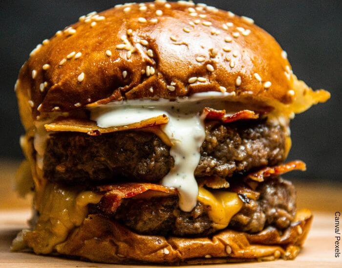 Foto de una hamburguesa doble carne con queso y tocino en primer plano para representar cuántas calorías tiene la comida chatarra