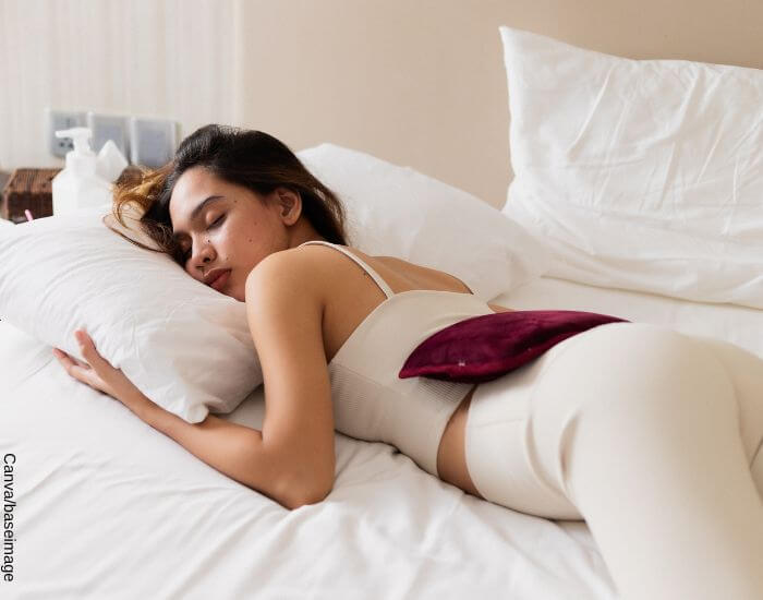 Foto de una mujer durmiendo con una bolsa de agua caliente en su espalda en representación de lo que sirve para los cólicos menstruales