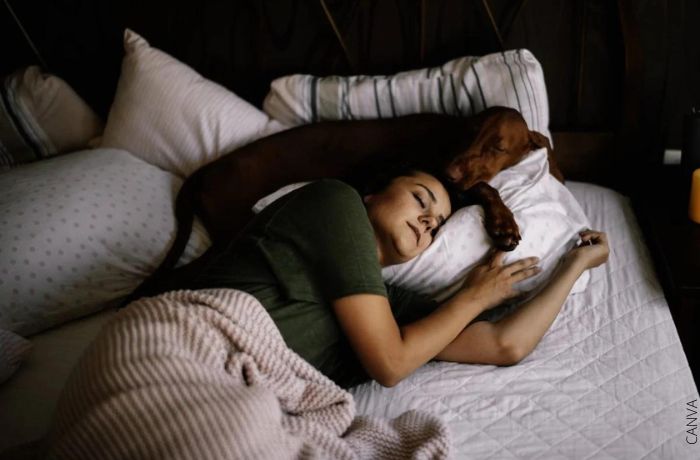 Foto de una mujer durmiendo con su perro en la cama