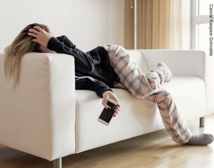 Foto de una mujer recostada en el sofá en pijama con el celular en la mano esperando a que él la llame