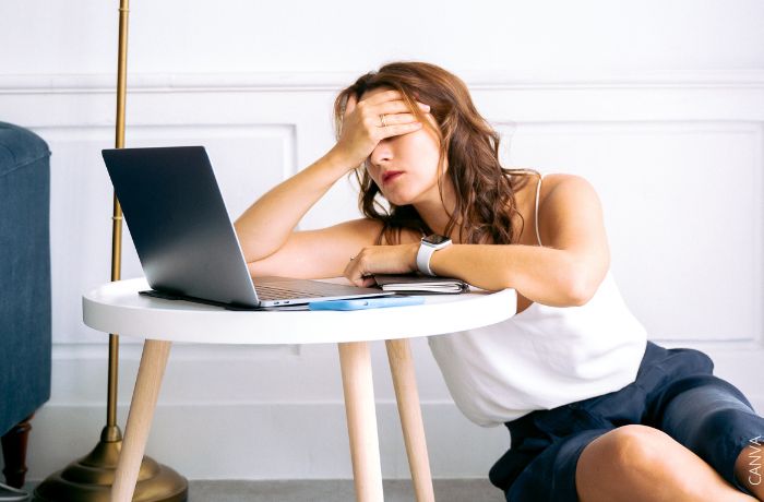 Foto de una mujer cansada con una mano en la cara y frente al computador