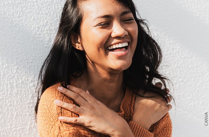 Foto de una mujer riendo con sus manos cruzadas en los hombros
