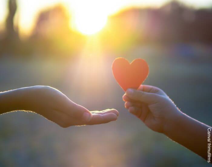 Foto de una mano regalando un corazón rojo de cartulina a otra mano