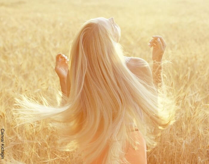 Foto de una mujer rubia de espaldas en medio de un campo de trigo dejando caer su largo pelo
