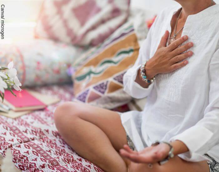 Foto de una mujer meditando con la mano en su pecho tocando uno de sus chakras espirituales
