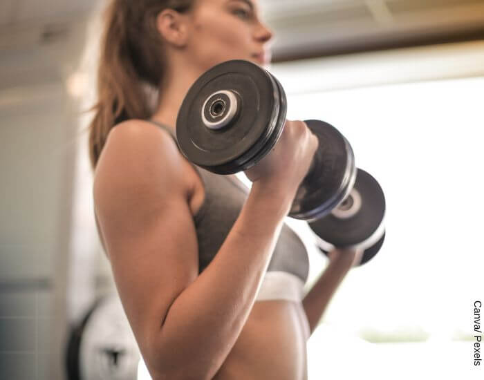 Foto de una mujer en top deportivo haciendo pesas en representación de por qué los senos duelen con ejercicio