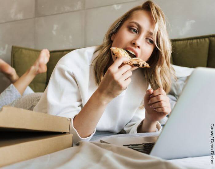 Foto de una mujer comiendo pizza mientras mira una serie en su portátil sola