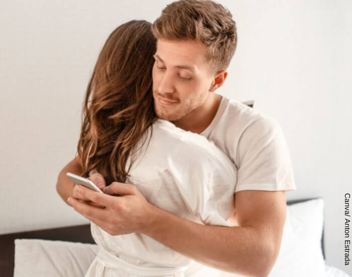 Foto de una pareja abrazada mientras el hombre usa su celular a escondidas para representar las mentiras más populares de los hombres casados