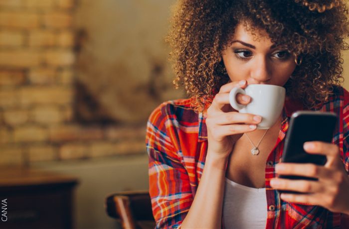 Foto de una mujer mirando su celular mientras toma café
