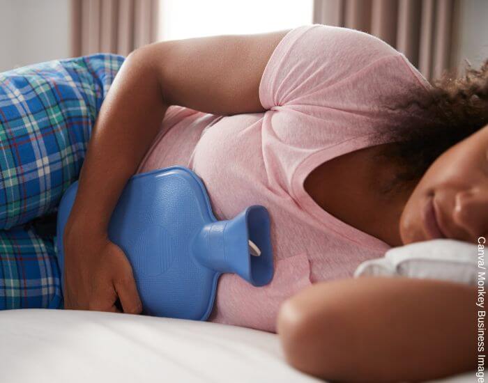 Foto de una mujer recostada sosteniendo una bolsa de agua caliente contra su abdomen en representación de lo que es bueno para los cólicos menstruales