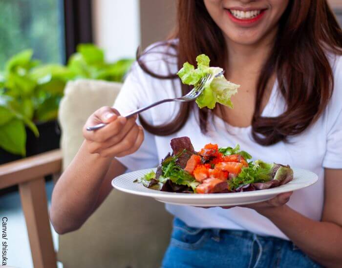 Foto de una mujer comiendo un plato de ensalada y pescado como una de las dietas para bajar de peso
