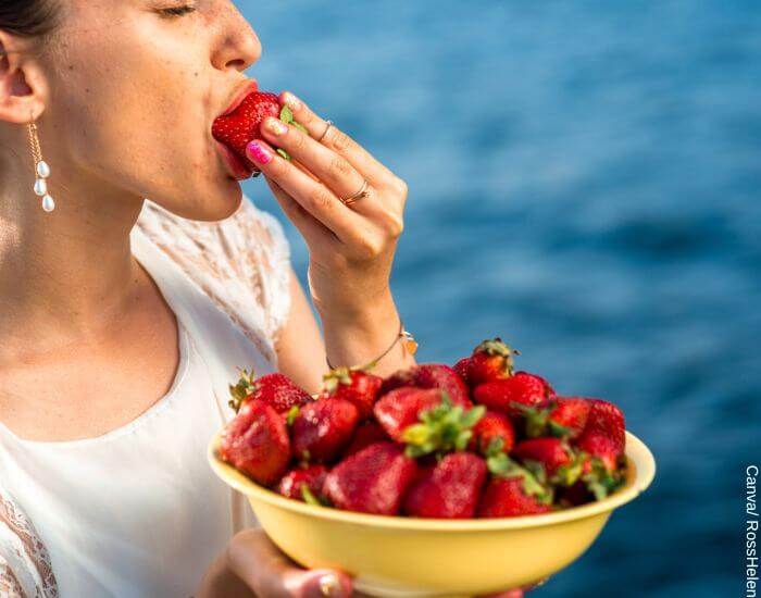 Foto de una mujer comiendo un plato de fresas junto al mar como parte de una de las dietas para bajar de peso