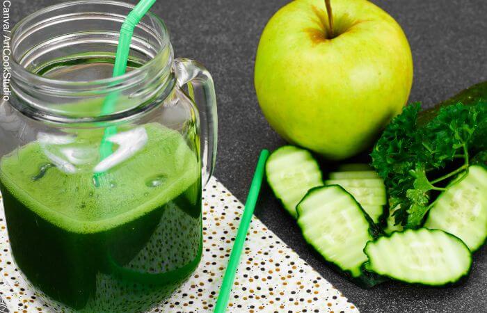 Foto de un pepino picado en rodajas, una manzana verde, un poco de perejil y un vaso de jugo verde para adelgazar