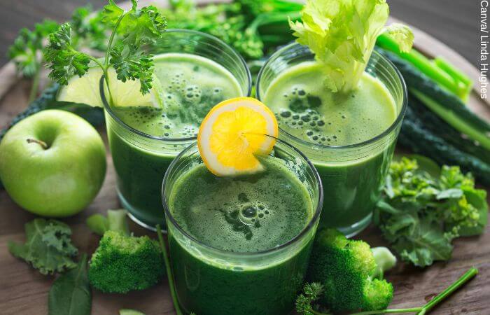 Foto de 3 vasos de jugo verde rodeados por los ingredientes como lechuga, brocoli, limón y manzana