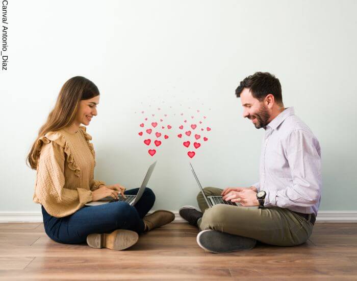 Foto de una pareja hablando vía computador con corazones brotando de sus pantallas para representar los mensajes de amor distancia