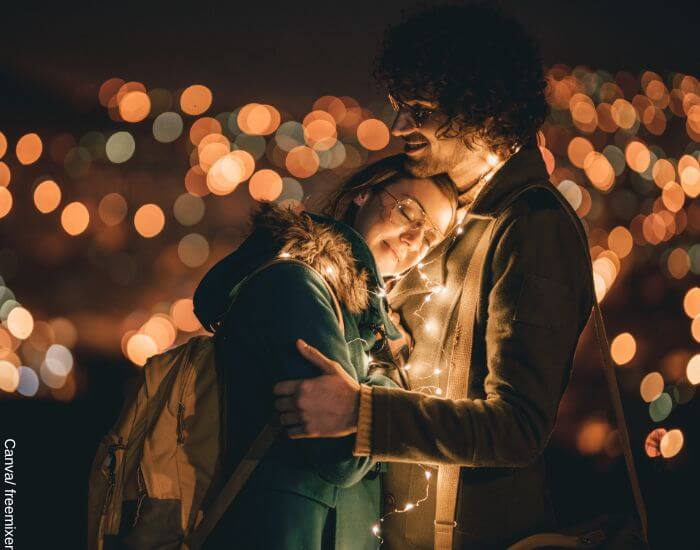 Foto de una pareja abrazada en medio de la noche con luces navideñas sobre sus cuerpos