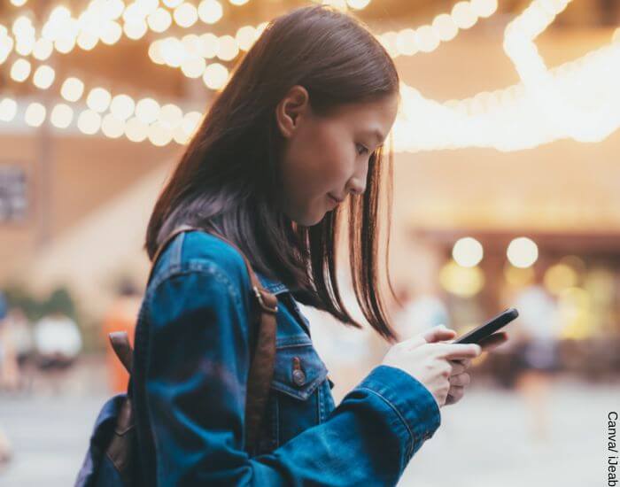 Foto de una mujer mirando su celular en la calle porque está enviando mensajes de amor a distancia a su pareja