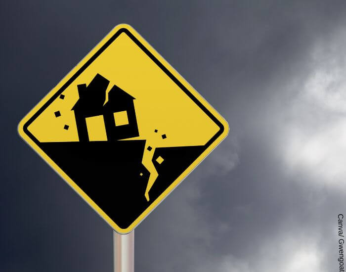 Foto de una señal de sismo amarilla con una casa agrietada y piso agrietado para representar el soñar con temblor