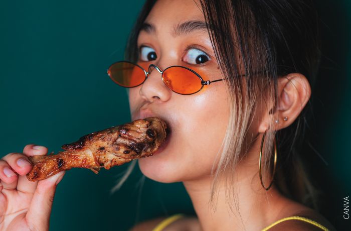 Foto de una mujer con una presa de pollo en la boca