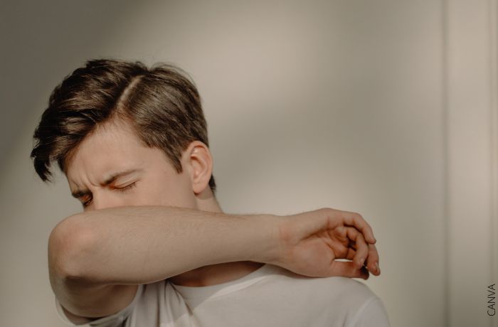 Foto de un hombre tosiendo en su brazo