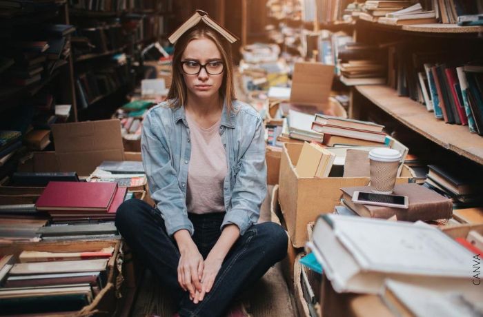 Foto de una mujer con un libro en la cabeza en medio de muchos libros