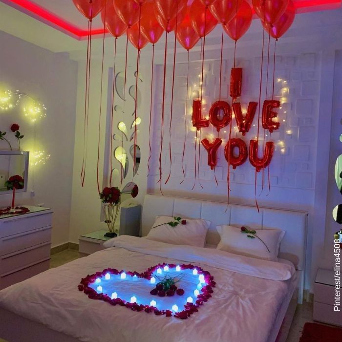 Foto de una cama decorada con un corazón de petalos de rosas y luces