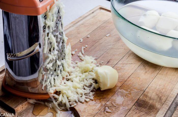 Foto de un queso a medio rallar con papas al fondo