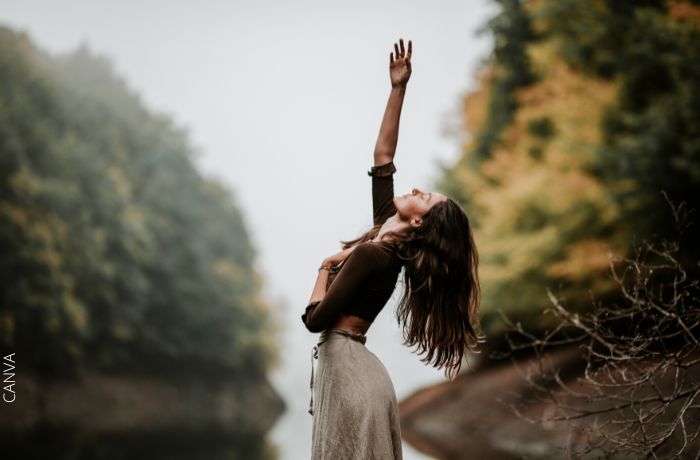 Foto de una mujer con la mano levantada en medio de la naturaleza