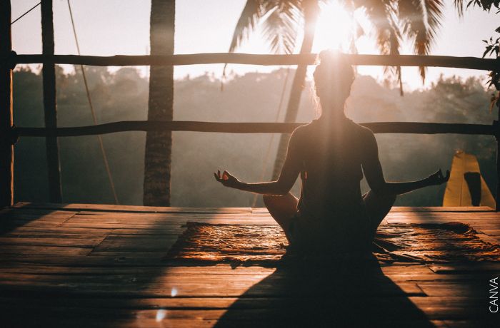 Foto de una mujer frente al sol en posición de yoga